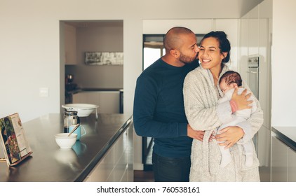 Loving Young Couple With Their Newborn Baby Boy In Kitchen. Beautiful Young Family Of Three In Morning In Kitchen.