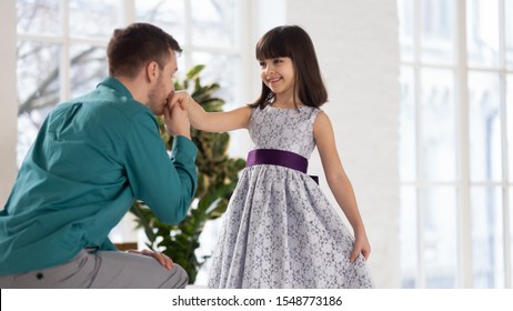 Loving Young Father Stay On One Knee Kiss Little Cute Daughter Wearing Beautiful Princess Dress Hand, Caring Father Gentleman Act Kneeling Near Smiling Small Preschooler Girl Child Show Good Manners