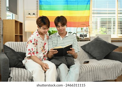 Loving young gay couple enjoy spending leisure weekend time together at home, reading book on couch - Powered by Shutterstock