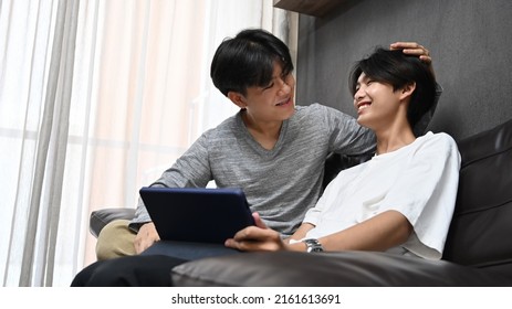 Loving Young Gay Couple Using Digital Tablet Together In Living Room. Concept Of Sexual Freedom And Equal Rights For LGBT Community