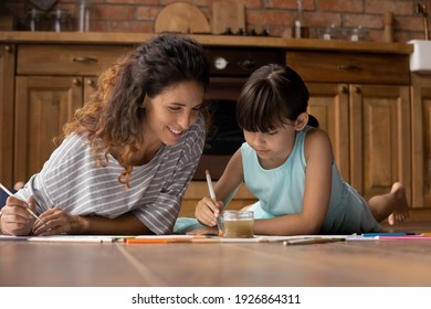 Loving Young Hispanic Mom And Little 9s Daughter Lying On Floor At Home Drawing Together In Album. Caring Latino Mother And Small Girl Child Have Fun Painting, Engaged In Hobby Activity On Weekend.