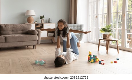 Loving young Indian mother raise on outstretched arms her cute little 6s daughter, family play together, dreaming about travel feel untroubled and happy. Leisure, games with children at home concept - Powered by Shutterstock