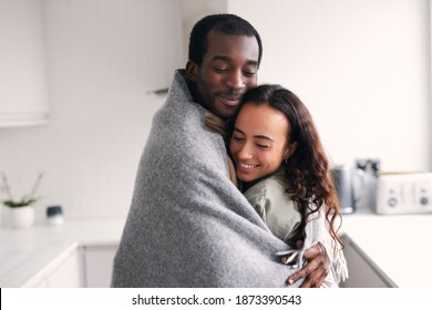 Loving Young Mixed Ethnicity Couple Cuddling Whilst Standing In Kitchen Wrapped In Cosy Blanket Together