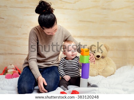 Loving Young Mom and her Cute Baby Boy Playing with Colored Plastic Blocks at Home.