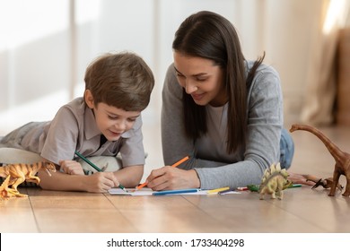 Loving young mom nanny lying warm floor drawing in album and little boy child  smiling mother have fun play paint paper and small son home family weekend  children creativity concept