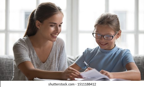 Loving Young Mother Help Smiling Small Daughter Prepare School Assignments At Home, Caring Mom Study With Teen Clever Girl Child Wearing Glasses, Do Homework Lesson Preparation Together