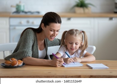 Loving Young Mother And Little Preschooler Daughter Sit At Table Drawing On Paper Together, Caring Mum Or Nanny Playing With Small Girl Child, Paint Pictures In Notebook, Early Development Concept