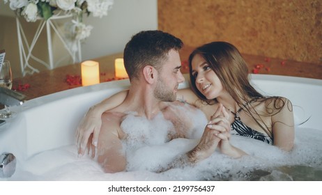 Loving young people in bathing suits are talking, hugging and touching hands in hot bathtub in spa salon. Romantic relationship, passion and wellness concept. - Powered by Shutterstock