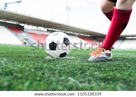 Low angle action shot of unrecognizable teenage boy forcefully kicking ball during football match on outdoor stadium, copy space