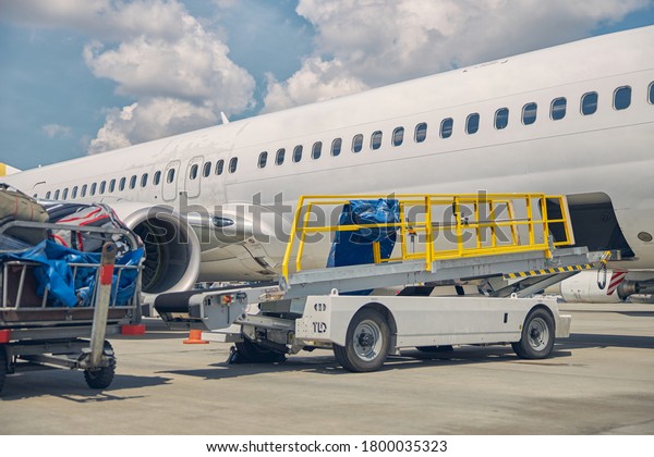 Low angle of an airport baggage\
loader vehicle standing in front of the newly arrived\
airliner