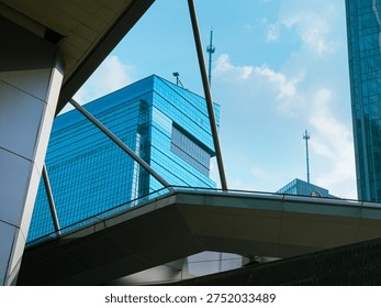 Low angle architectural view of modern glass office buildings and skyscrapers with geometric lines under a blue sky with soft clouds.