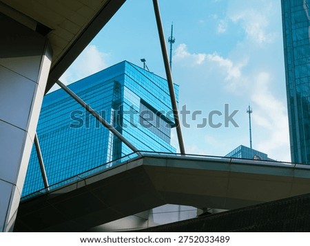 Low angle architectural view of modern glass office buildings and skyscrapers with geometric lines under a blue sky with soft clouds.