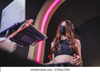 LOW Angle Asian Woman Dj Wear Black Mask Play The Music On The Mixing Console In The Nightclub, Asian Female In Mask Turn Up Music In The Club During Covid-19, Live Performance, Anti-quarantine