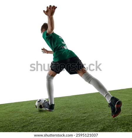 Low angle back view image of teen boy, soccer player in green jersey and black shorts in motion on field, kicking ball against white background. Concept of sport, education, competition, game