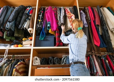 Low angle back view of unrecognizable female picking outfit hanging on rail with different clothes in closet
