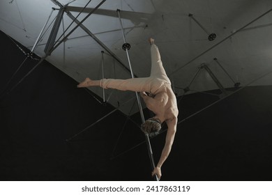 Low angle back view of unrecognizable topless man performing pole dance element holding on to pylon with twisted grip in upside down position