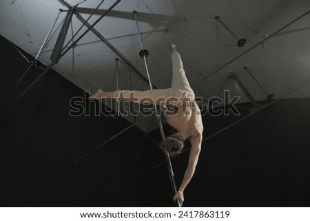 Low angle back view of unrecognizable topless man performing pole dance element holding on to pylon with twisted grip in upside down position