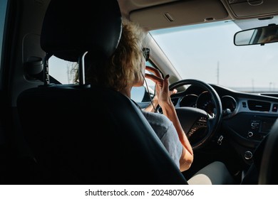 Low Angle Backseat View Of A Woman Driving Her Car. She's Touching Her Lips.