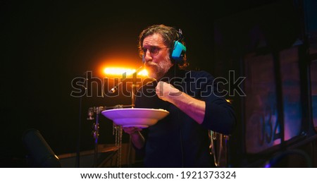 Low angle of bearded mature male sound designer chewing food and speaking in microphone while creating soundtrack for film in studio