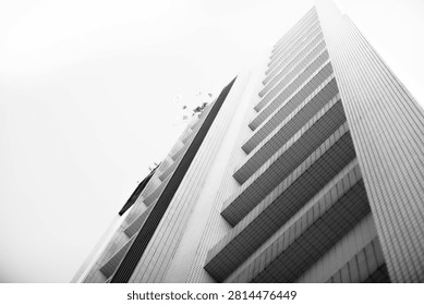Low angle black and white view of a modern high-rise building with repeating balconies, tiled walls and strong geometric lines against a bright sky