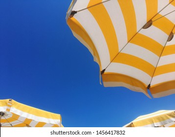 Low angle bottom view and detail of yellow and white beach or poolside umbrellas with a blue sky in the background - holiday and vacation concept - Powered by Shutterstock