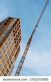 Low Angle Building Construction and Tower Crane. Low-angle view of a high-rise building under construction with a tower crane against blue sky, symbolizing urban growth.