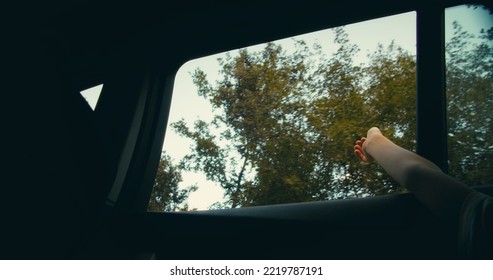 Low Angle From Car Interior Child Hand Out Of Vehicle Window On Road Trip. 