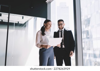 Low angle of cheerful coworkers in formal clothes standing near window and looking at documents while working together in modern office - Shutterstock ID 2278263929