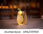 Low angle close up of ice cold modern gourmet craft cocktail of gin and tonic soda garnished by lemon slice and rosemary sprig sprinkled by juniper berries on bar with blurry restaurant bar background