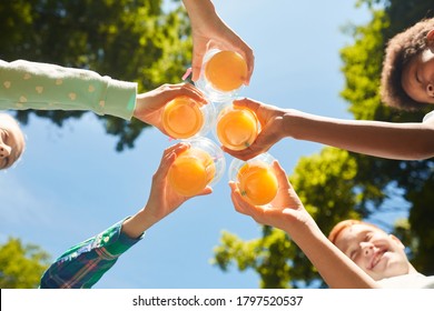 Low angle close up of kids holding glasses with orange juice against blue sky outdoors, copy space
