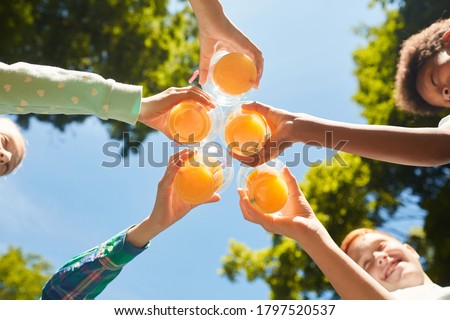 Low angle close up of kids holding glasses with orange juice against blue sky outdoors, copy space