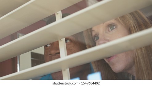 Low angle Close up of nosy older married couple looking out the window. African American husband and wife shot through the window and blinds of their house - Powered by Shutterstock