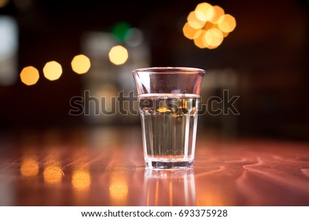 Low angle close up perspective of crystal clear traditional Italian wine glass with drinking cup shape filled with white wine on wood counter top bar with blurry lights and restaurant background