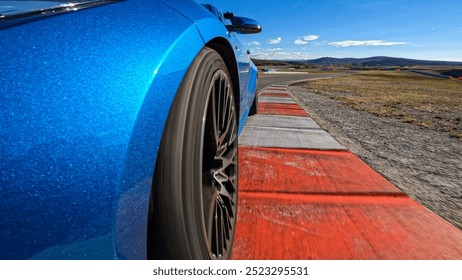LOW ANGLE, CLOSE UP: Cool wheel shot of a sportscar speeding down racetrack during race. Metallic blue sports car racing on a closed circuit during a track day sparkles in the bright autumn sunshine.
