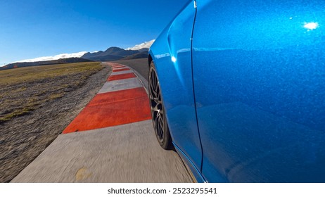 LOW ANGLE, CLOSE UP: Cool shot of a brand new sports car racing on a closed track on a perfect sunny afternoon. Sparkling metallic blue sportscar speeds along the empty circuit on a perfect autumn day