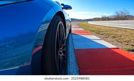 LOW ANGLE, CLOSE UP: Cool curb shot of a metallic blue car racing down the asphalt track on a sunny autumn day. Sportscar speeds along a sweeping circuit turn with a striking red and white curb.