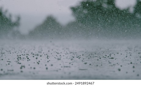 LOW ANGLE, CLOSE UP, DOF: Cinematic shot of hail falling on the asphalt during a heavy tropical rainstorm. Small pellets of ice fall on the wet concrete ground during hailstorm on a gloomy summer day.
