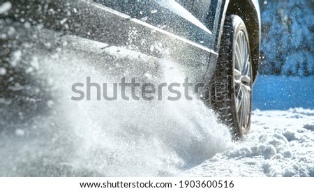 LOW ANGLE, CLOSE UP, DOF: Fresh snow flies up from a large vehicle's spinning wheel. Car's wheels spin and spew up pieces of snow and snowflakes as it attempts to gain traction on the slippery road. ストックフォト © 