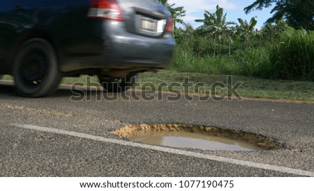 LOW ANGLE, CLOSE UP: Gray car evades a gaping water filled pothole on remote concrete road on exotic island. Car drives past a dangerous hole in the damaged asphalt street leading through rainforest.