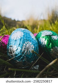 Low angle close up view of tin foil covered chocolate easter eggs in grass with sky in the distance
