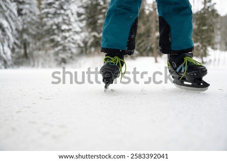 Low angle closeuo view of a childs legs ice skating on a natural ice outside in snowy nature.