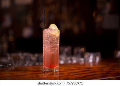 Low Angle Closeup Of A Gourmet Mixed Drink Cocktail Of Sweet Pink Lemonade Vodka And Gin Martini, Garnished By A Lemon Slice And Straw, On A Wood Grain Countertop