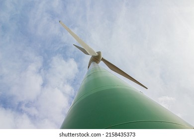 A Low Angle Closeup Of A Green Wind Turbine Under A Cloudy Sky