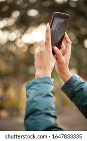Low angle and close-up image of hands holding smartphone and taking a photo of trees in nature at day time.  