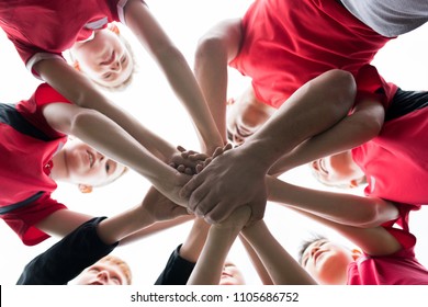 Low Angle Closeup Of Junior Football Team Stacking Hands During Motivational Pep Talk Before Match In Outdoor Stadium, Copy Space