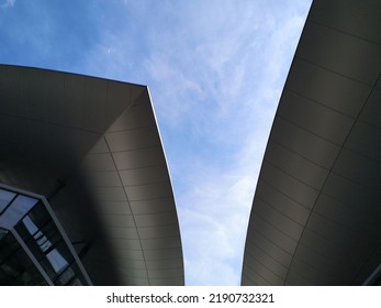 Low Angle Close-up Of Modern Building. Abstract Architecture And Material Design With Curvy Roof. Minimal Exterior Background With Curve Structure. Geometric Composition Of Curves Against Blue Sky.