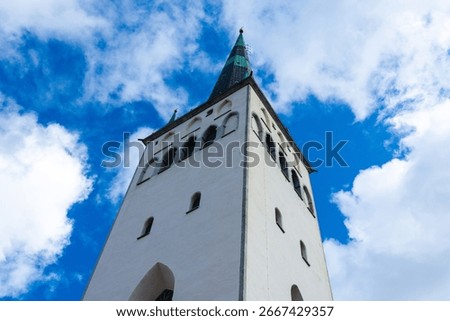 Low angle close-up of St. Olaf's Church in Tallinn, Estonia. The tall white tower and green spire rise against a vivid blue sky filled with scattered clouds.