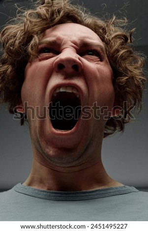 Low angle closeup studio portrait of enraged young Caucasian man with curly hair yelling