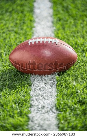 A low angle close-up view of a leather American Football sitting in the grass on a white yard line.