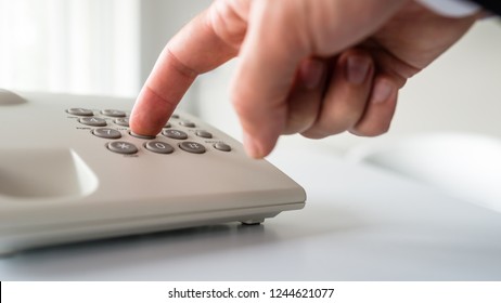 Low Angle Closeup View Of Male Hand Dialing A Phone Number On White Landline Telephone.